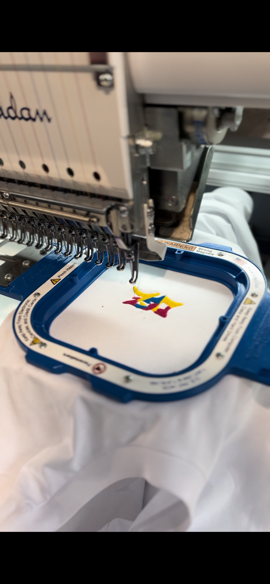 Machine à broder qui brode le logo DGZ multicolor sur un teeshirt blanc.