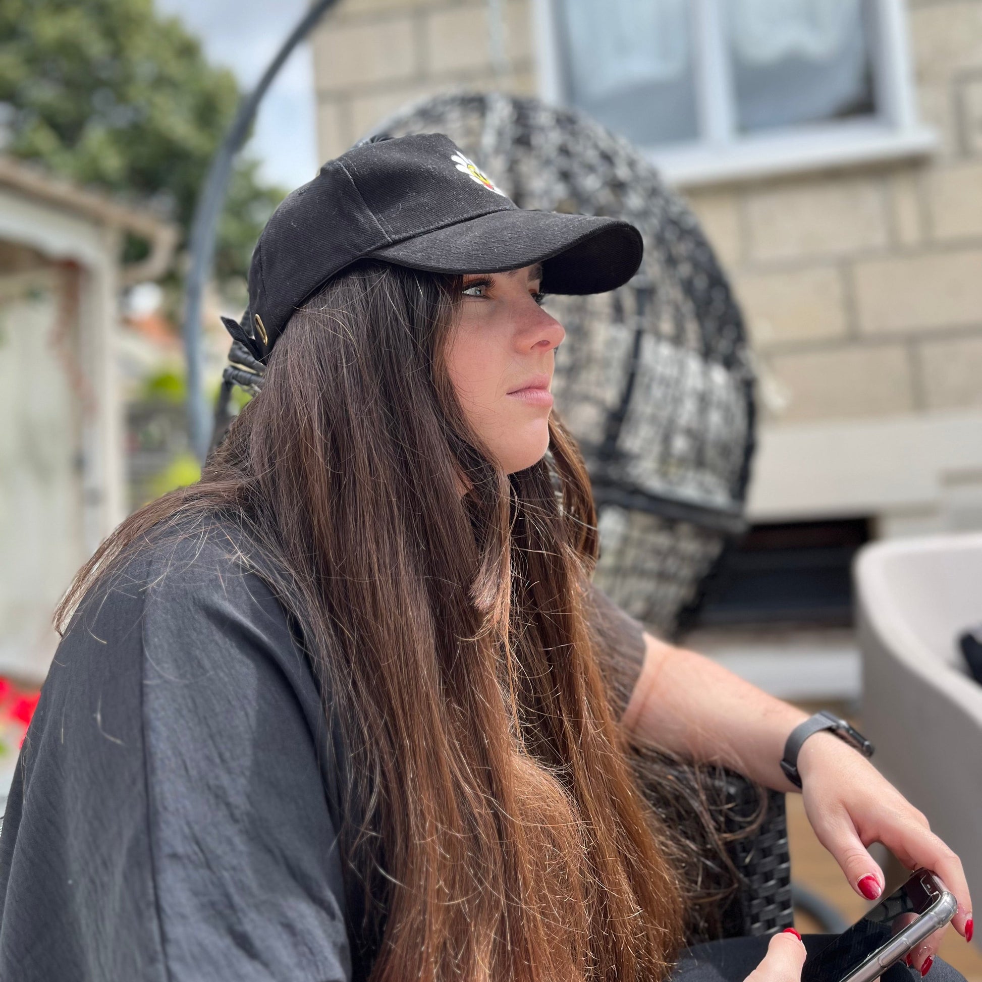 Une femme porte une casquette Daniel by DGZ en terrasse. La vue est de profil sur son côté droit. La femme, qui s'appelle Oréo, regarde au loin.